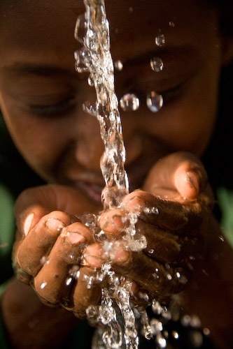 a young boy is playing with water from a faucet in his hands,