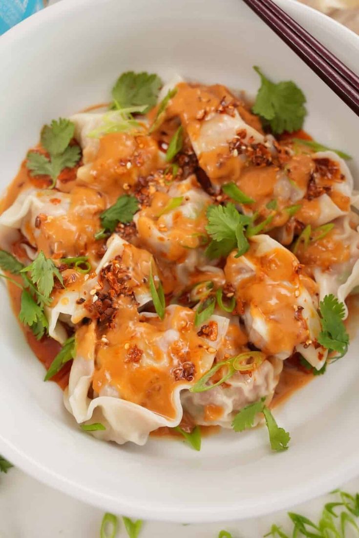 a white bowl filled with dumplings covered in sauce and garnished with cilantro