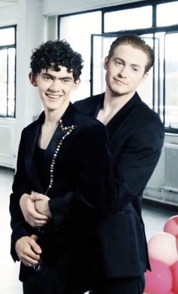 two young men standing next to each other in front of balloons and balloon garlands