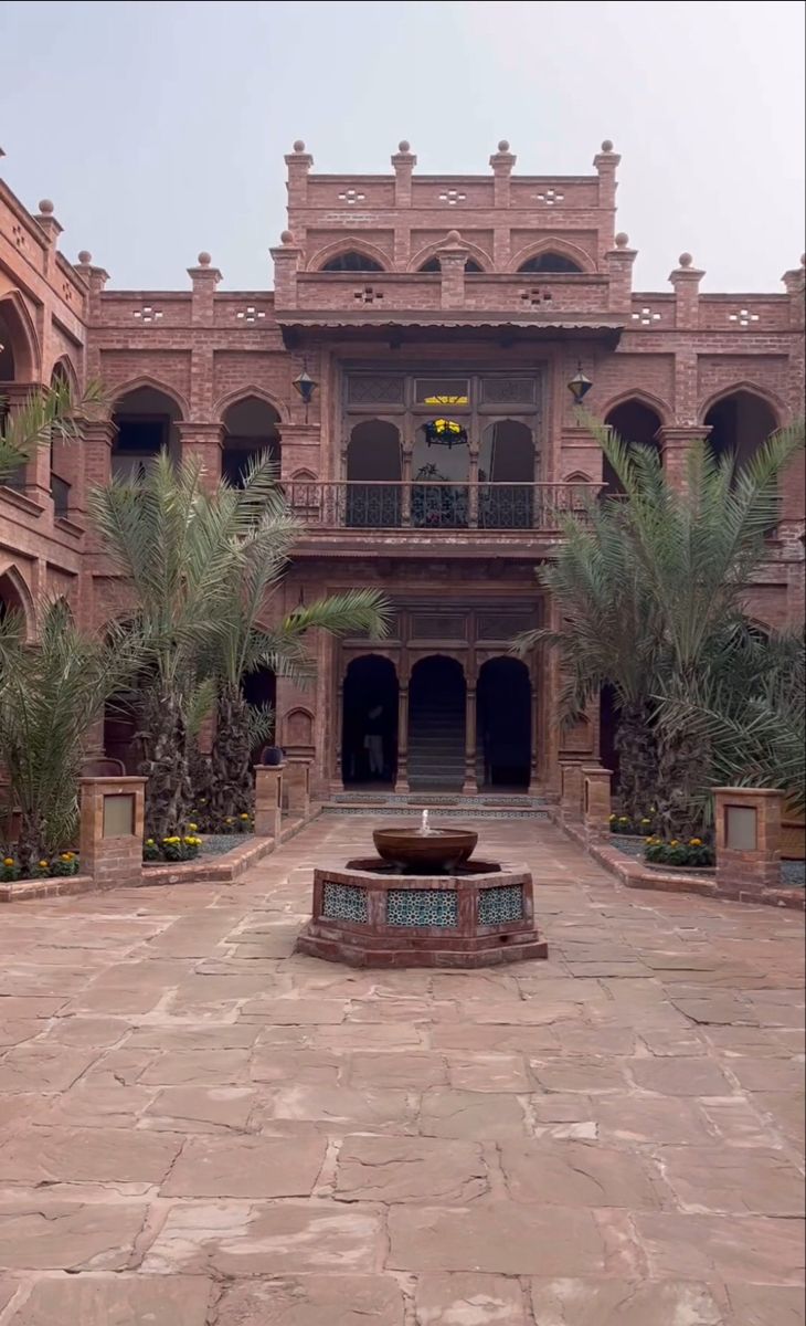 an old building with a fountain in the middle and palm trees on either side of it