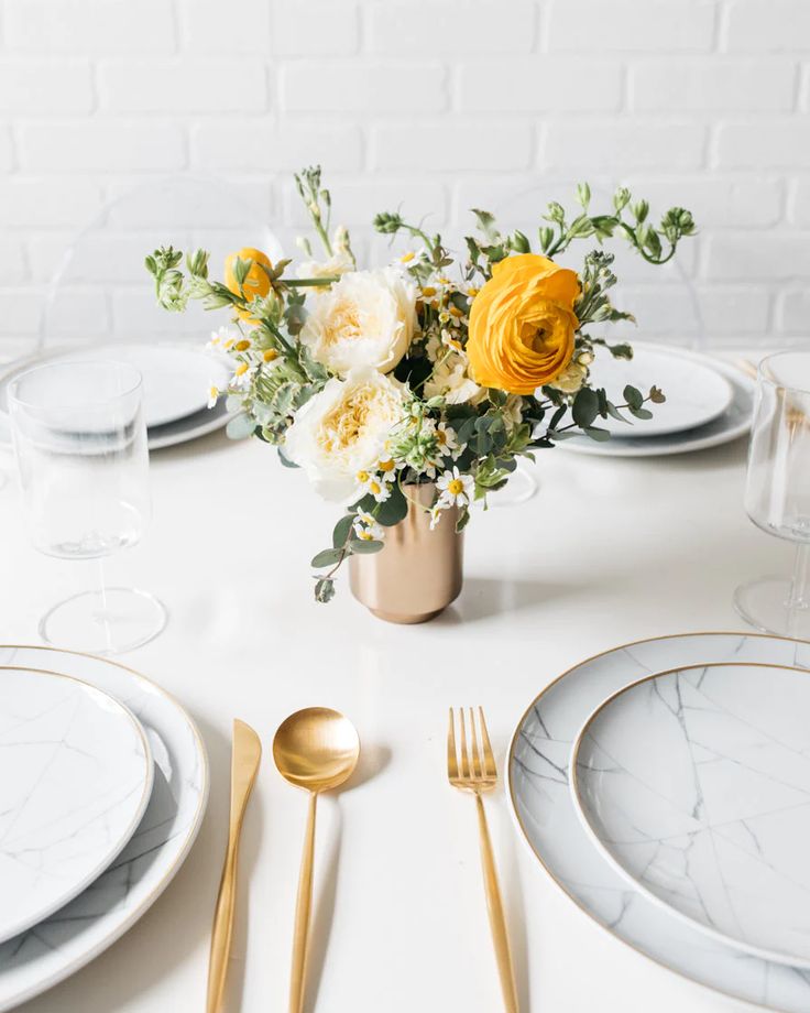 a white table topped with plates and silverware next to a vase filled with yellow flowers