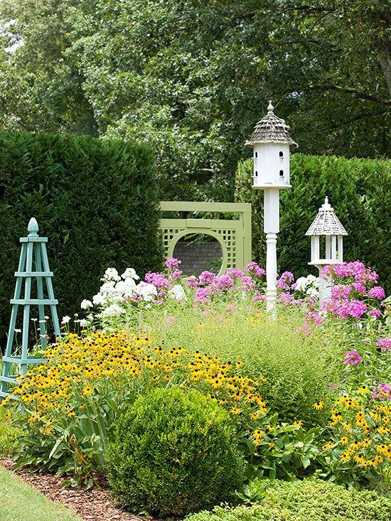 a garden filled with lots of flowers next to a tall white birdhouse on top of a lush green field