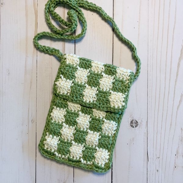 a green and white crocheted purse sitting on top of a wooden floor