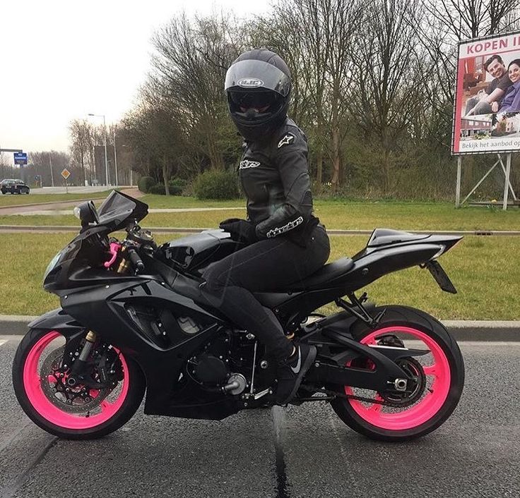 a person sitting on a motorcycle in the middle of the road with pink rims