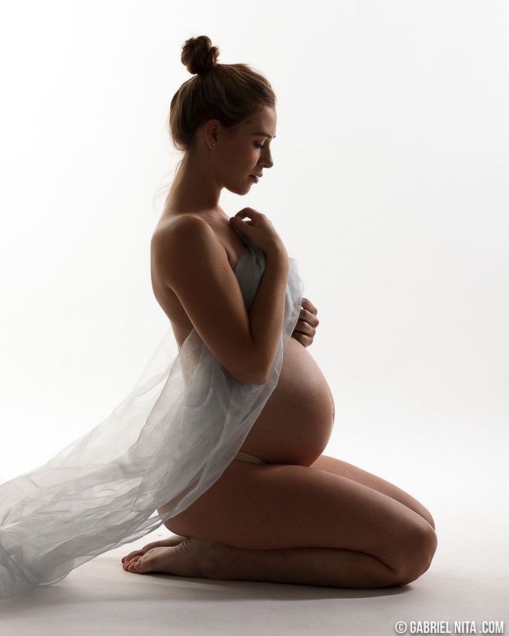 a pregnant woman sitting on the floor with her arms wrapped around her belly and looking down