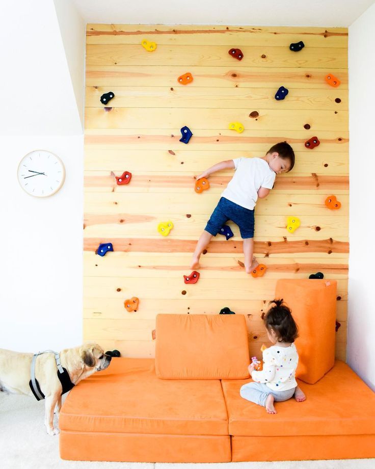 two children climbing up the side of a wall with an orange couch in front of them