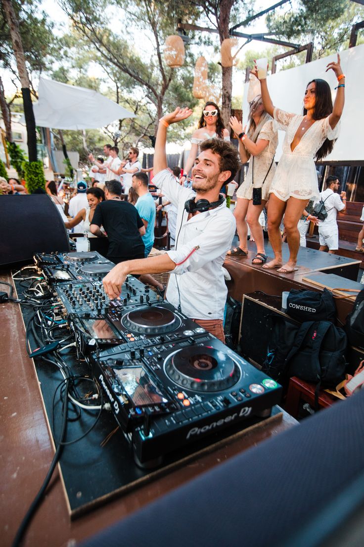 a dj mixing music at an outdoor event with people in the back ground and onlookers