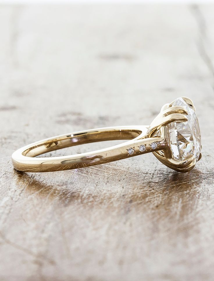 a yellow gold engagement ring with a large diamond in the center on a wooden surface