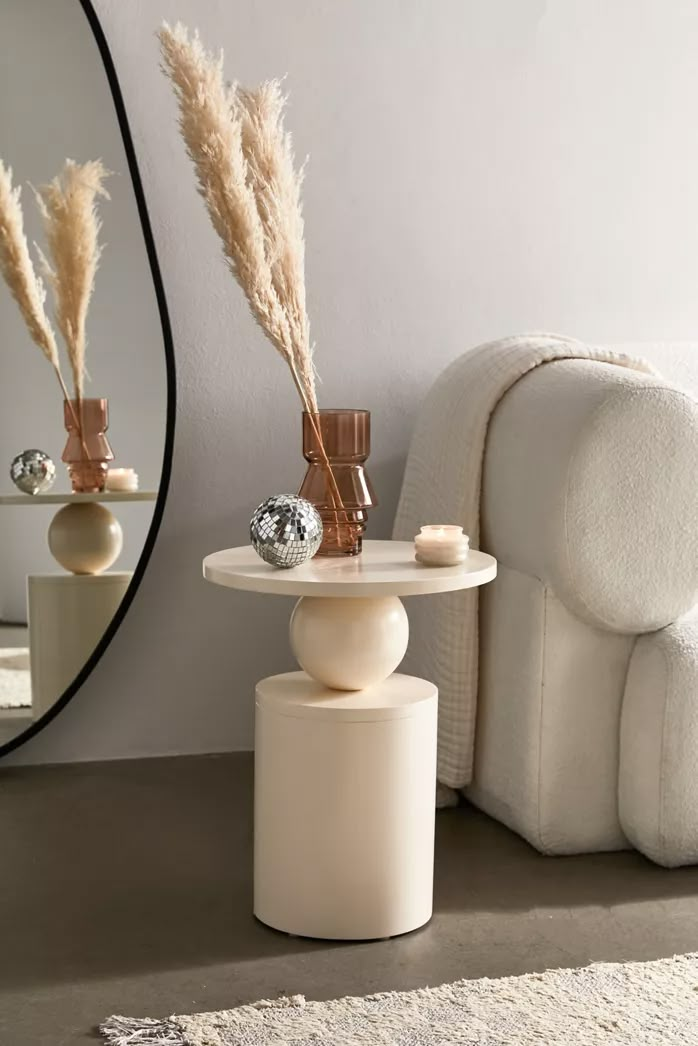 a mirror sitting next to a white chair and table with some plants on top of it