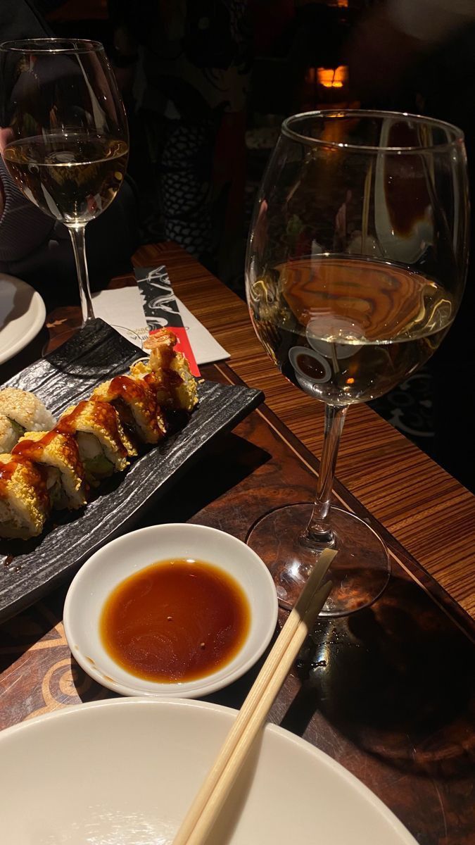 sushi and chopsticks on a table with wine