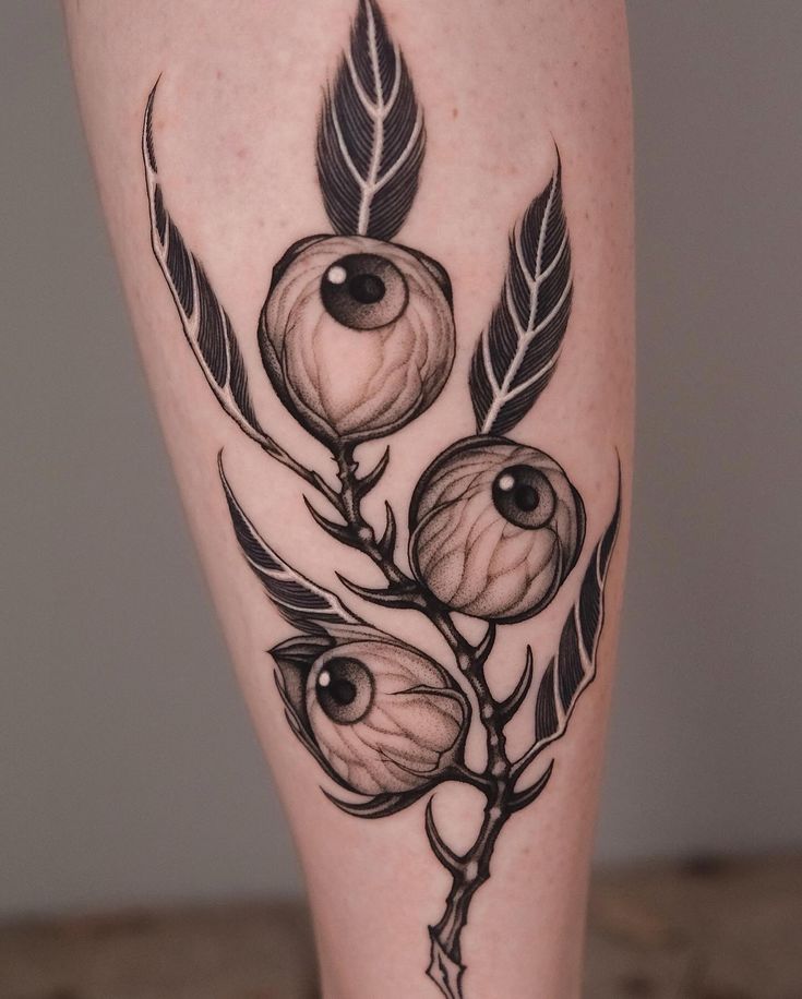 an artistic tattoo on the leg of a woman with flowers and leaves in black ink