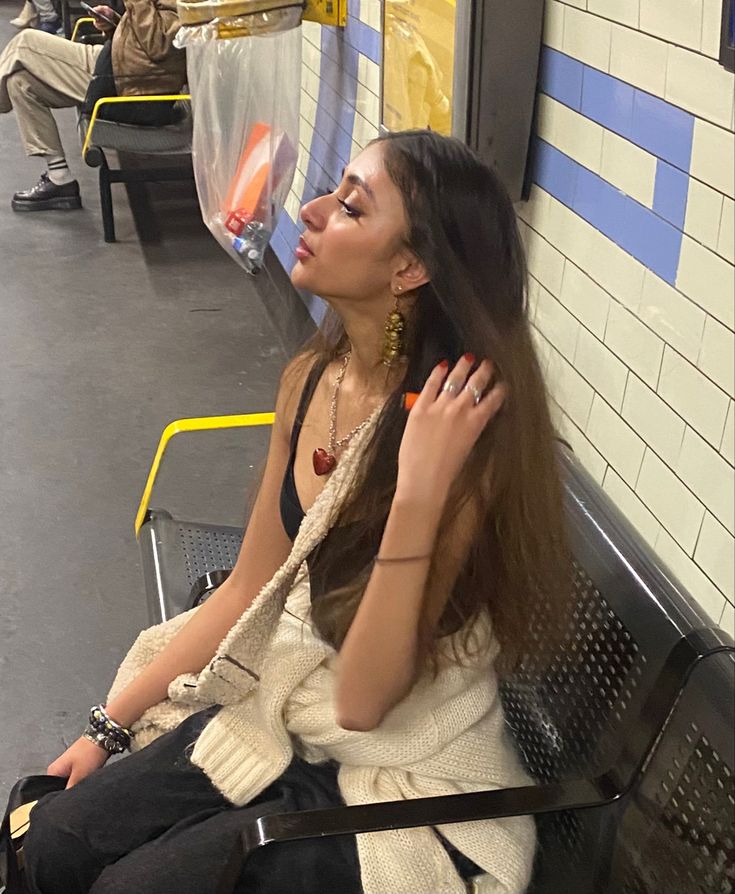 a woman with long hair sitting on a subway bench and talking on her cell phone