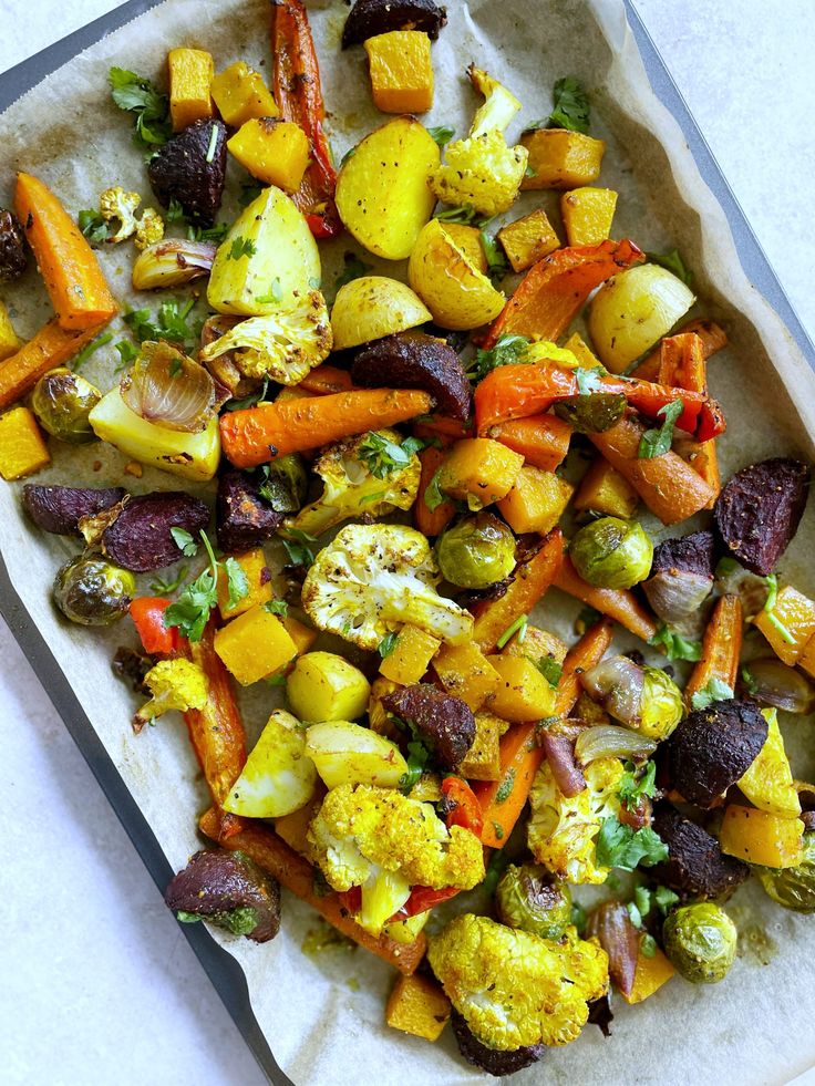 a tray filled with roasted vegetables on top of a white tablecloth covered in parchment paper