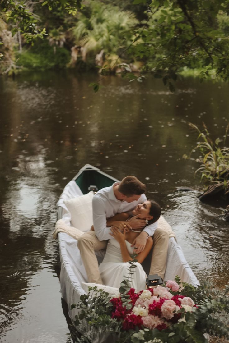 a man and woman are kissing in a boat on the water, surrounded by greenery