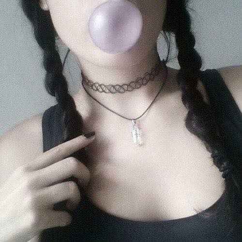 a woman blowing a bubble on her nose with a chain around her neck and wearing a black tank top