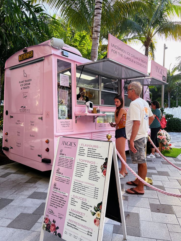 a pink food truck parked on the side of a road next to a palm tree