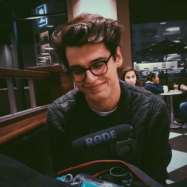 a young man wearing glasses sitting in front of a microphone and smiling at the camera