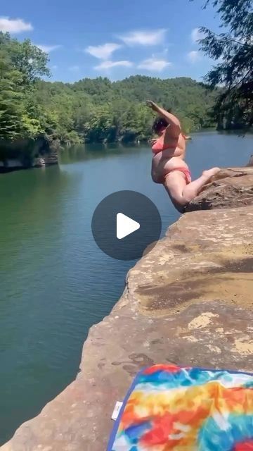 a person jumping off the edge of a cliff into a body of water with trees in the background