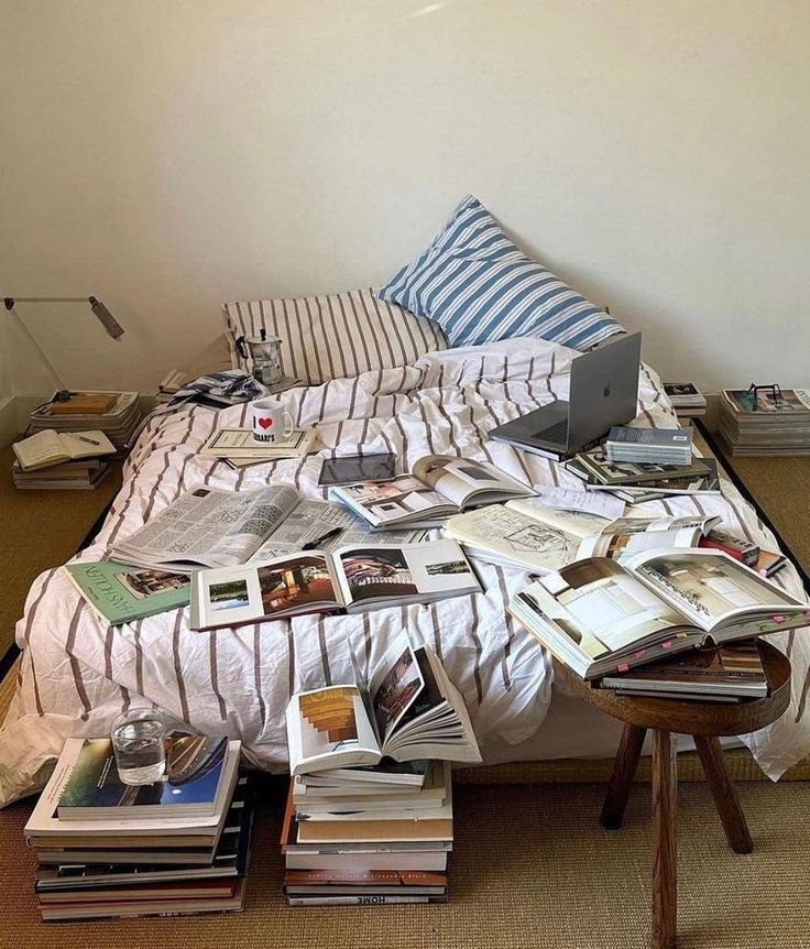 a bed covered in lots of books next to a desk with a laptop on it