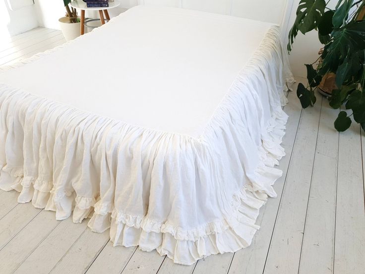 a white bed with ruffled bedspread on the floor next to a potted plant