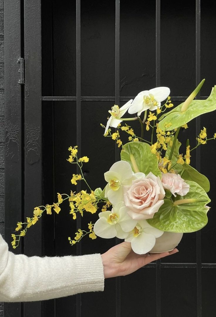 a person holding a bouquet of flowers in front of a black fence with yellow and white flowers