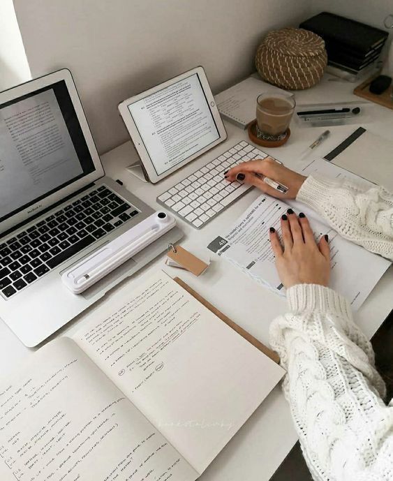 a person sitting at a desk with two laptops and papers on the table next to them