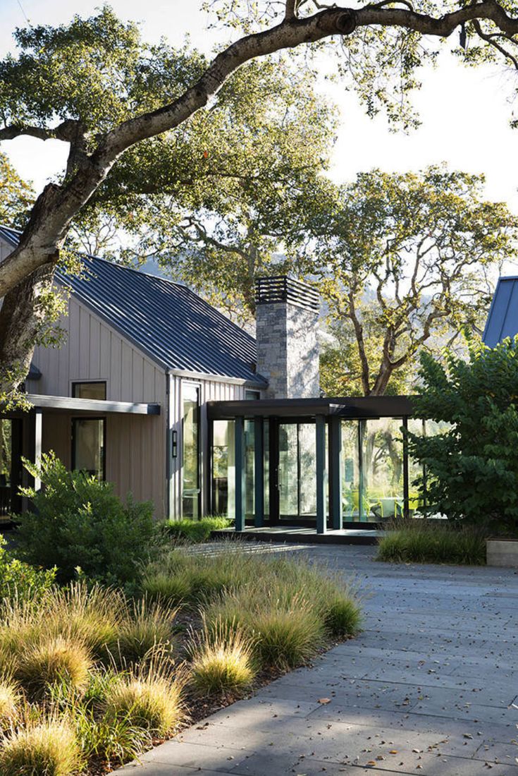 the house is surrounded by greenery and trees, with glass doors on both sides