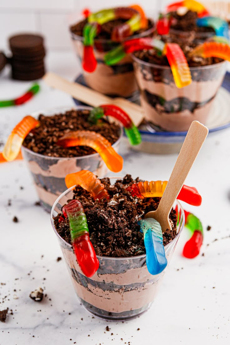 two desserts with gummy bears in them on a white counter top, one is filled with dirt and the other has candy