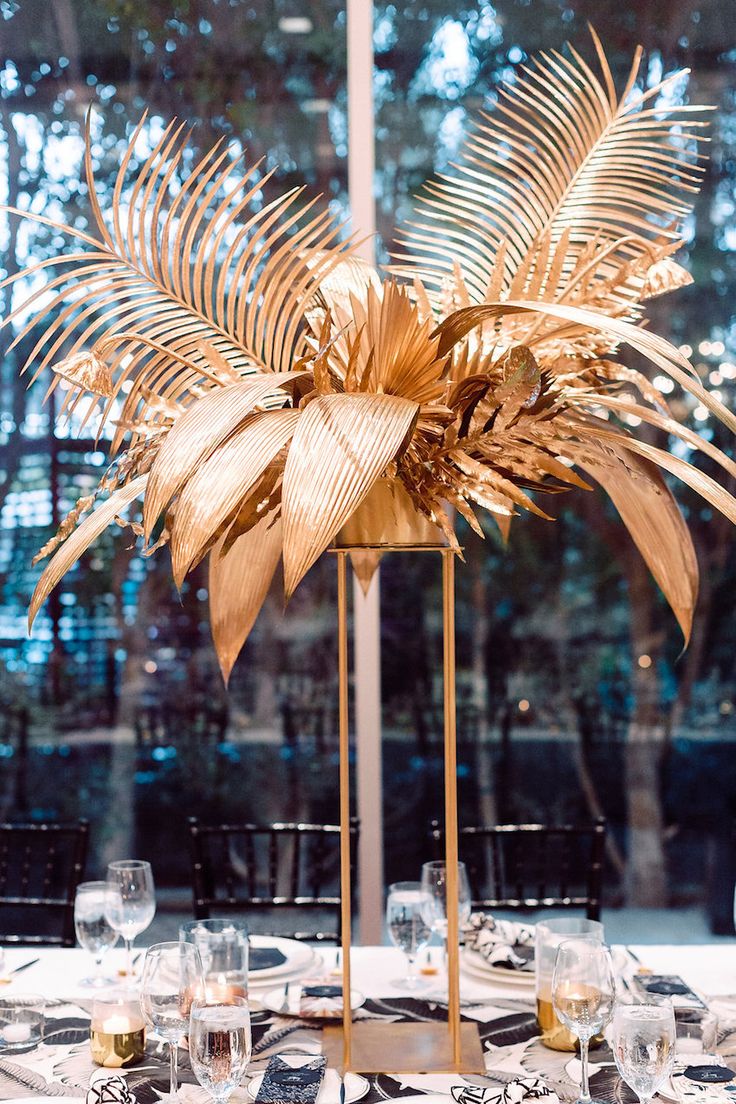 the table is set with white plates and silverware, gold leaf centerpieces