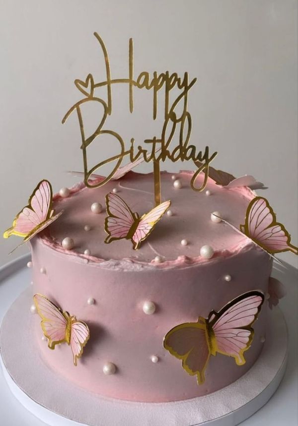 a birthday cake with pink frosting and gold butterflies