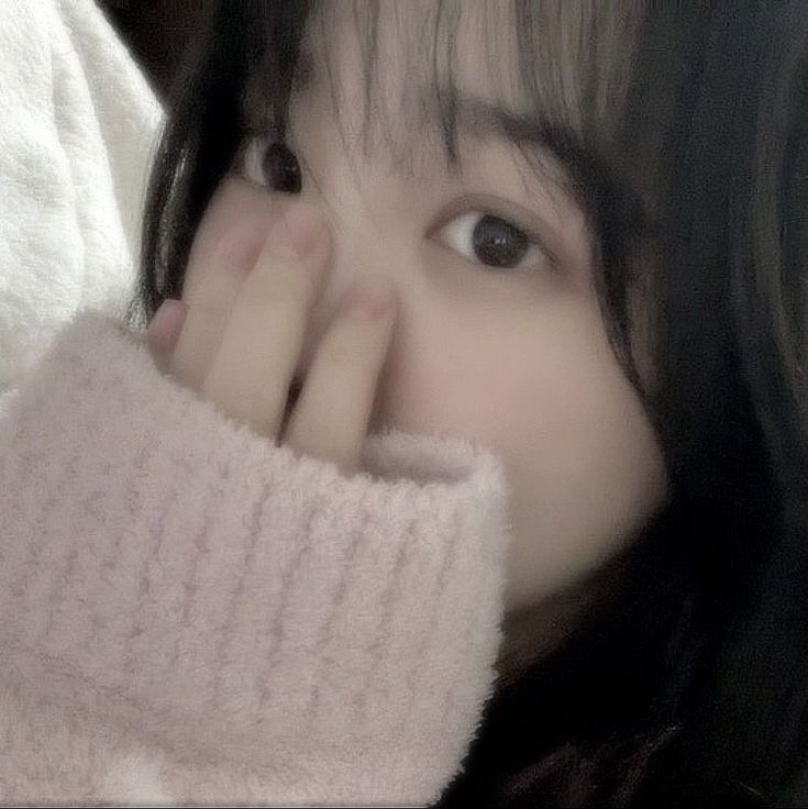 a woman with long black hair wearing a pink sweater and holding her hand up to her face