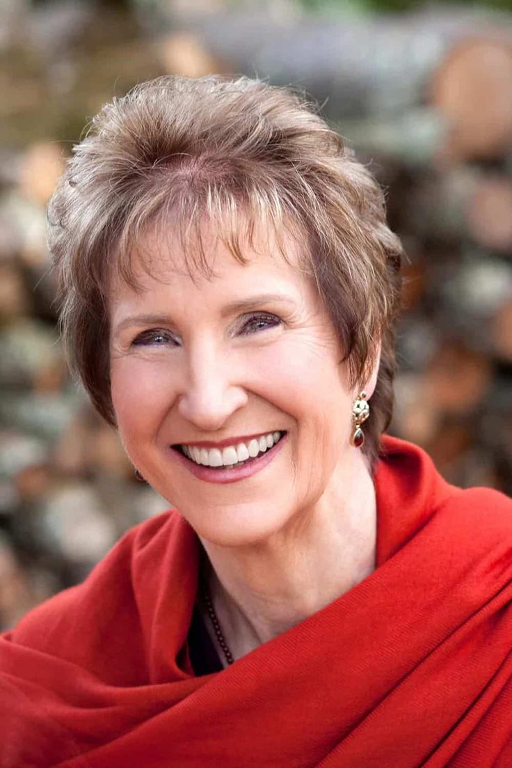 a smiling woman wearing a red shawl in front of some rocks and trees with her eyes closed