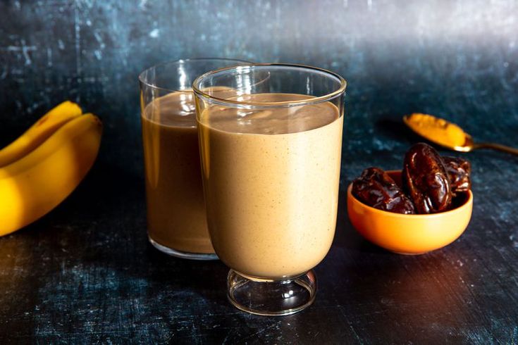 two glasses filled with chocolate pudding next to bananas and spoons on a black table