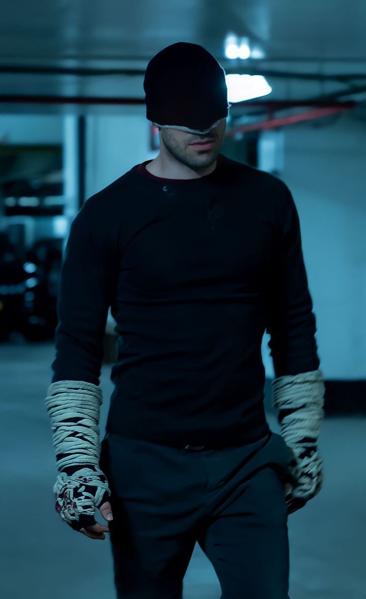 a man wearing gloves and a black hat is standing in a dark room with his hands on his hips