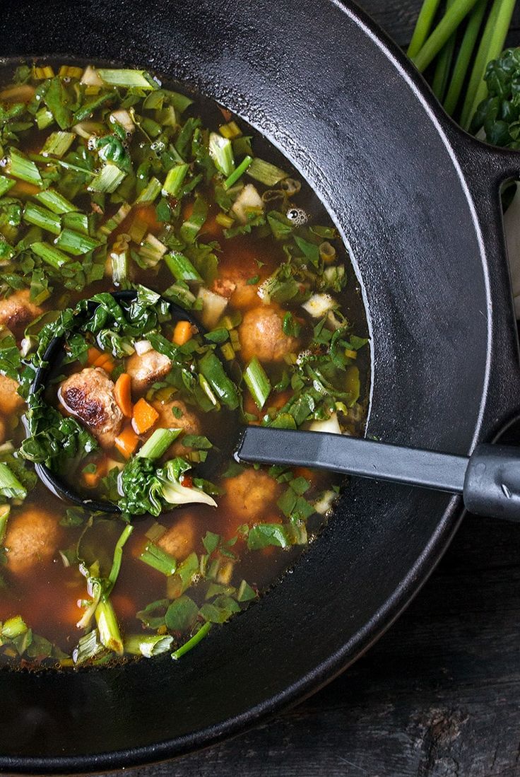 a pan filled with soup and vegetables on top of a wooden table