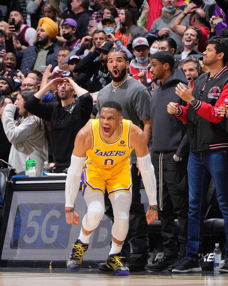 a basketball player is running on the court with his hands in the air as people look on