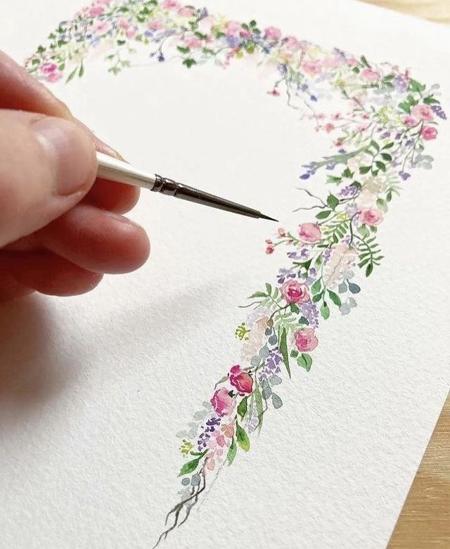 someone is drawing flowers on the paper with a pen and watercolors are in front of them