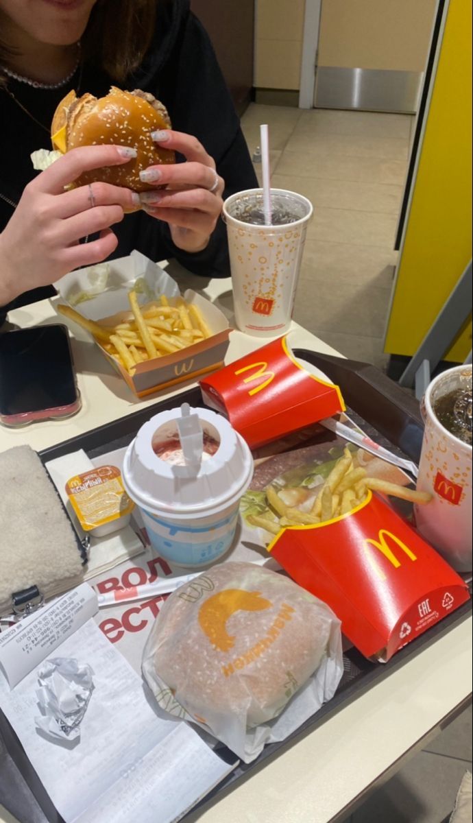 a woman sitting at a table eating a hamburger and french fries with ketchup