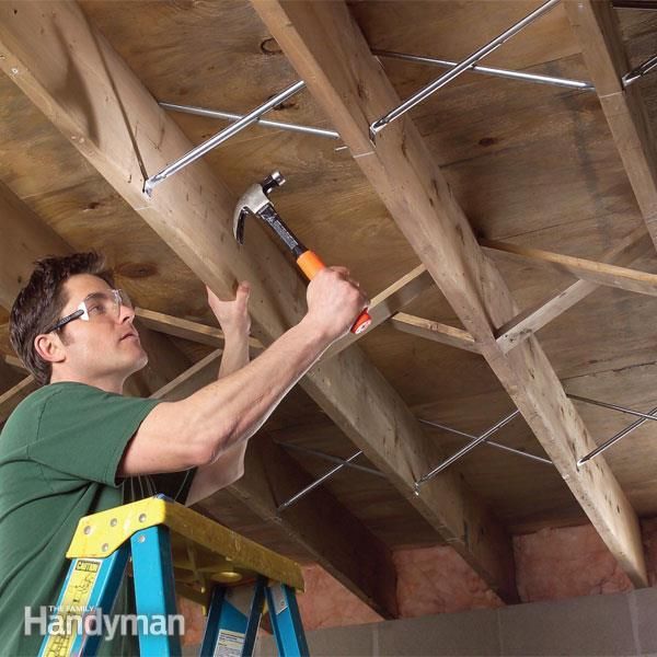 a man holding a hammer while standing on a ladder in a room with wooden beams