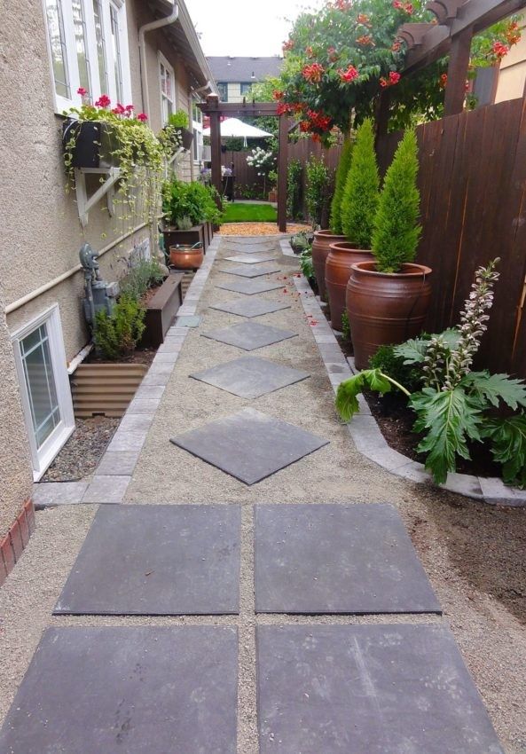 a long narrow walkway between two buildings with potted plants on each side and another planter in the background