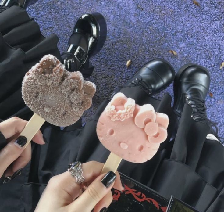 two people are eating pops on the ground with their feet in black shoes and one is holding a pink lollipop