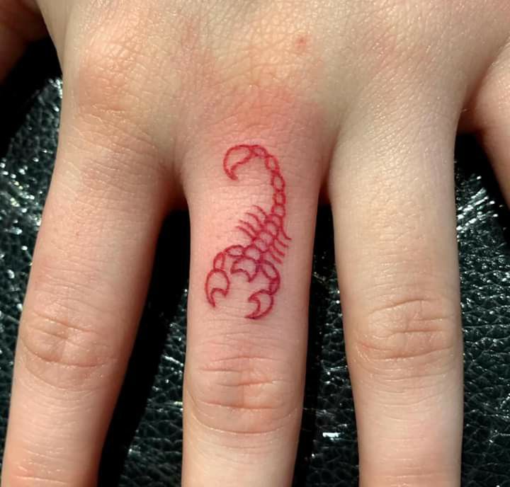 a woman's hand with a small scorpion tattoo on the middle finger and red ink