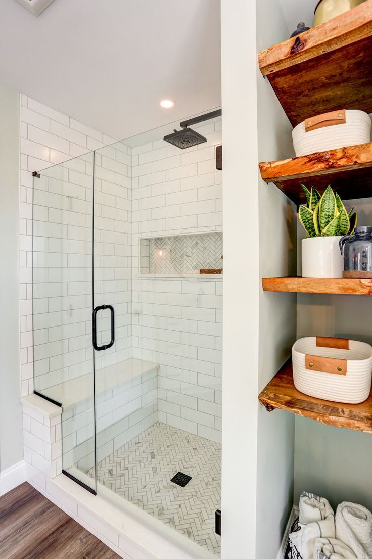 As the focal point of the room, a  freestanding bathtub sits below a large window providing natural light. With the large double vanity, makeup vanity, and exposed shelves, there is no shortage of storage. The beautiful tile shower boasts a tile accent design on the floor and in the niche, and a convenient bench is enclosed in a sleek glass shower door. Shiplap walls, matte black fixtures, and wooden accents are small touches that really bring it all together. Shower No Tub Ideas Bathroom, Bench In Small Shower Ideas, Shower With Bench And Shelves, Bathroom With No Bathtub, Bathroom Shower With Shelves, Glass Shower In Small Bathroom, Shower With Side Shelves, Double Shower Small Bathroom, Small Bathroom Ideas Glass Shower Door