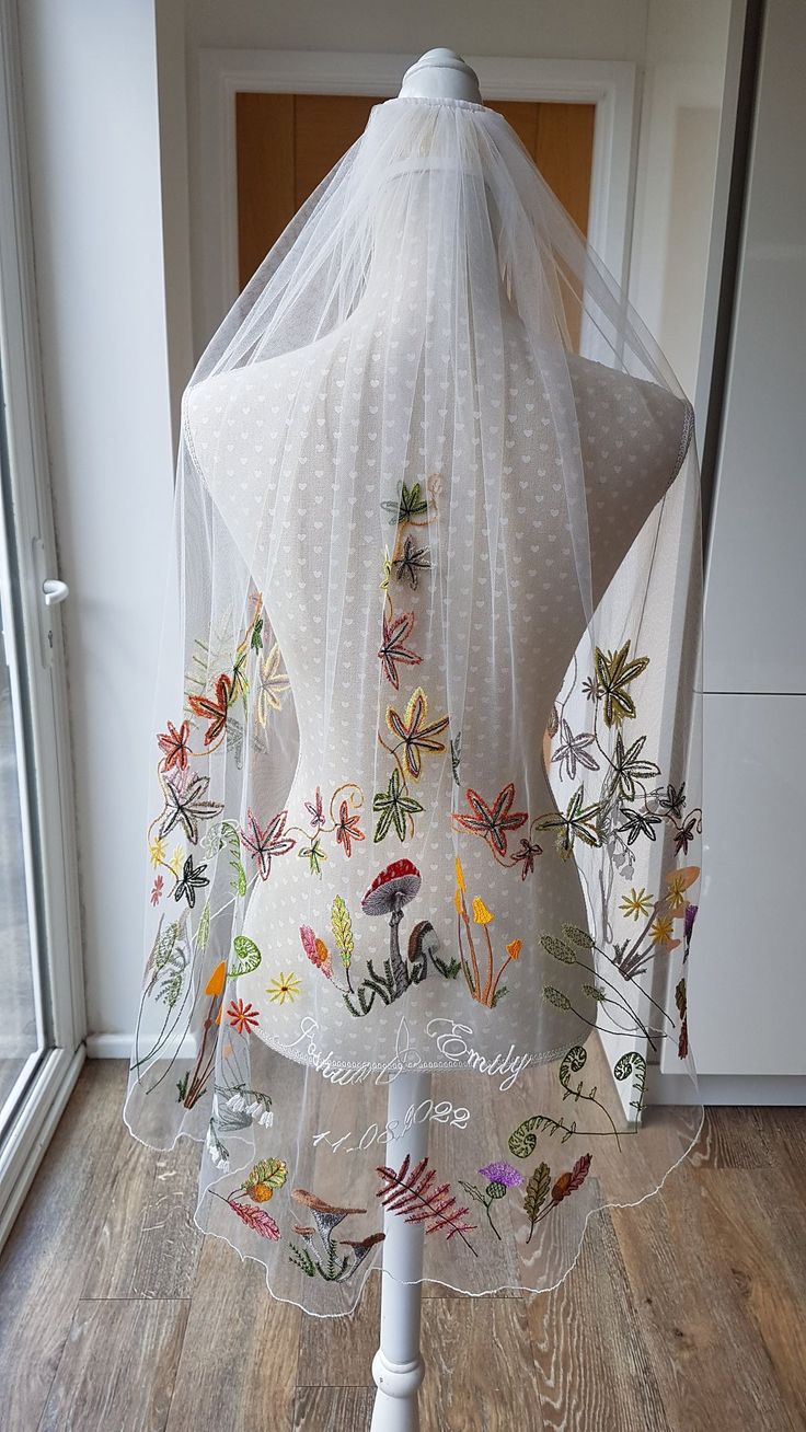 a white veil with embroidered designs on it sitting on top of a mannequin