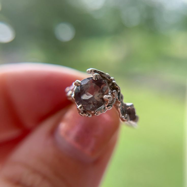 a close up of a person's hand holding a ring with a stone in it