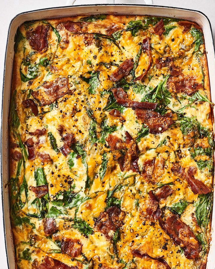 a casserole dish with spinach, bacon and cheese in it on a white surface