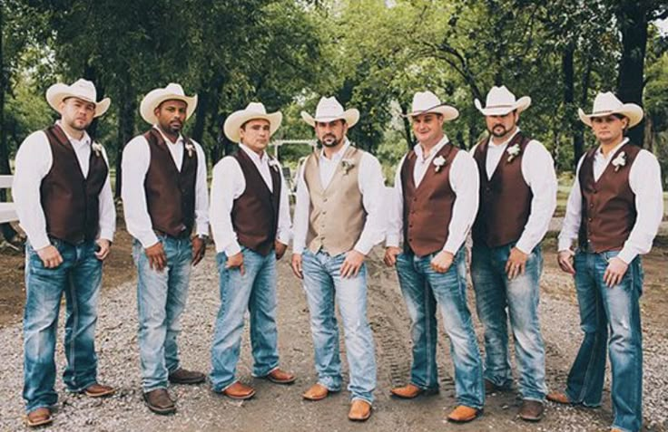 a group of men standing next to each other wearing cowboy hats and vests in front of trees