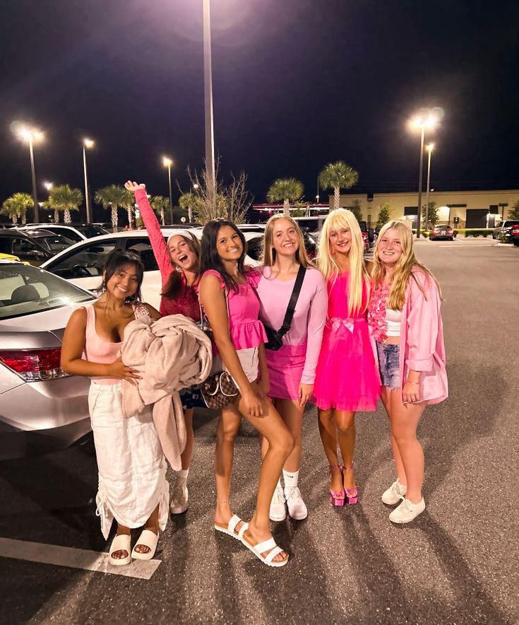 four girls are posing in front of a car at night with their arms around each other