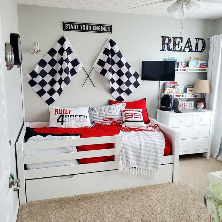 a white bed with red and black pillows on top of it in a bedroom next to a window