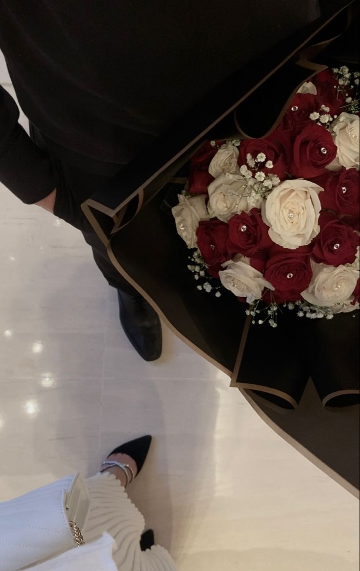 a bouquet of red and white flowers is being held by someone's hand on the floor